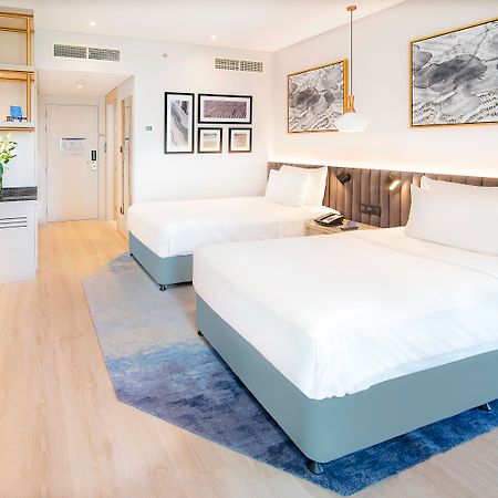 Radisson Blu Hotel & Resort, Abu Dhabi Corniche Екстериор снимка The image shows a modern hotel room featuring two double beds with white linens. The room has a light and airy ambiance, with wooden flooring and a complementary area rug. There are decorative wall frames with artwork above the beds, and a stylish pe