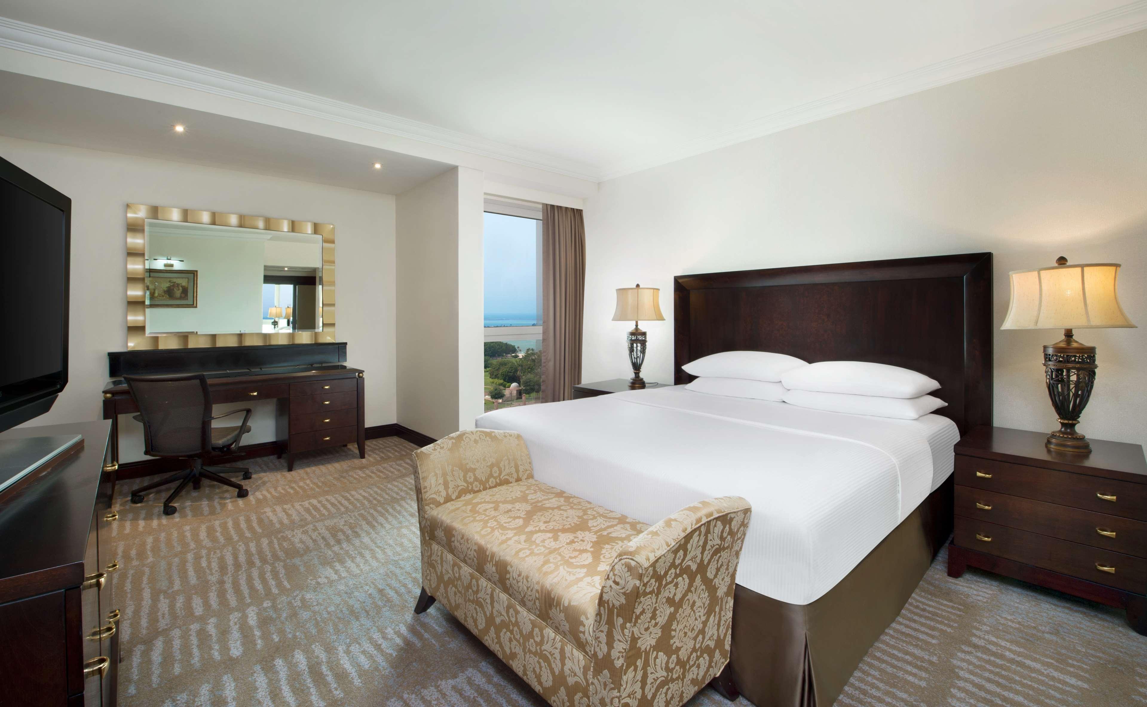 Radisson Blu Hotel & Resort, Abu Dhabi Corniche Екстериор снимка The photo shows a well-decorated hotel room featuring a comfortable king-sized bed with crisp white linens. There’s a stylish armchair at the foot of the bed. To one side, there's a desk with a chair, providing a workspace. A large mirror with a deco
