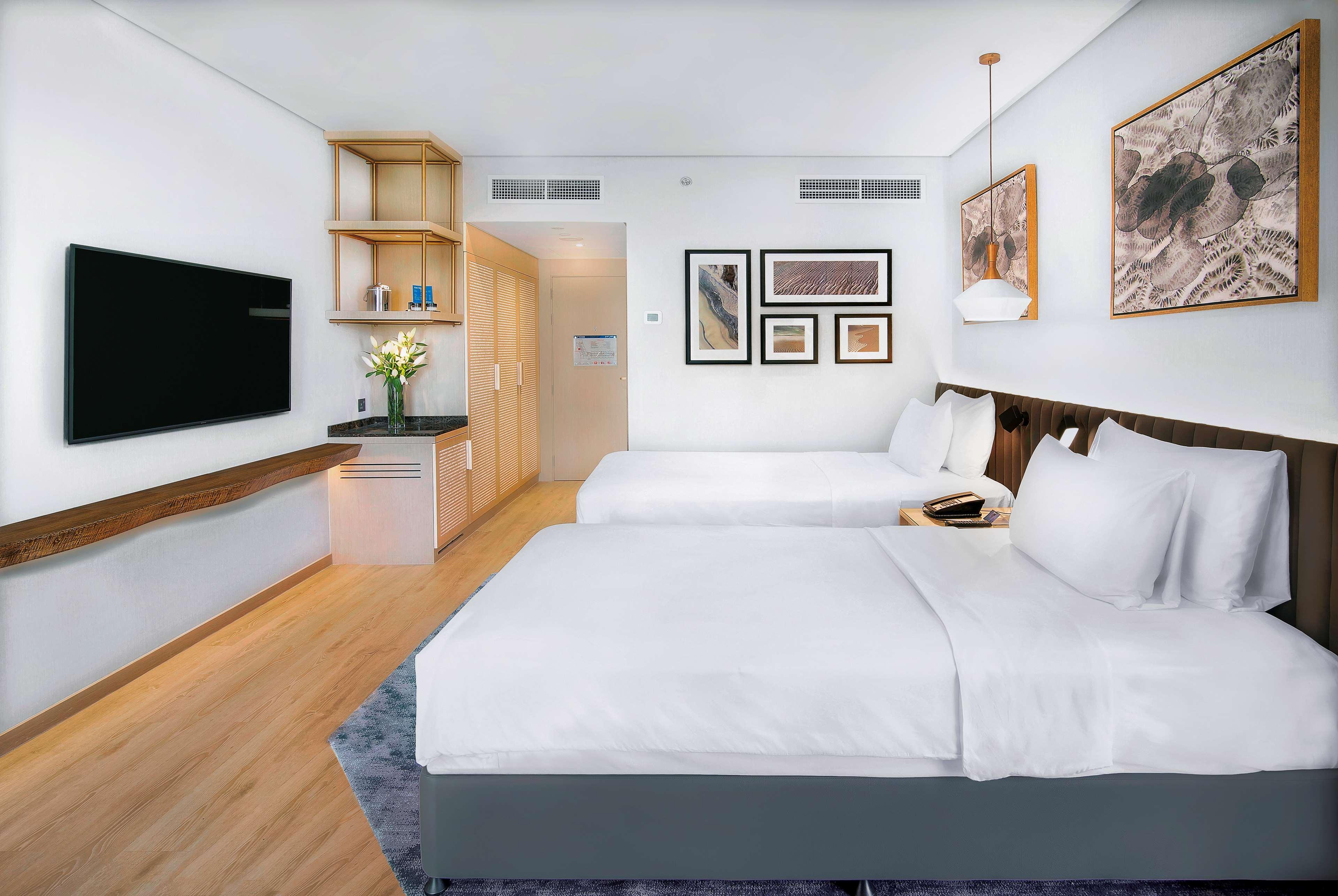 Radisson Blu Hotel & Resort, Abu Dhabi Corniche Екстериор снимка The photo shows a modern hotel room featuring two beds with white bedding. There's a flat-screen TV mounted on the wall opposite the beds. The room has light-colored wooden flooring and a large window, allowing natural light to enter. A small kitchen