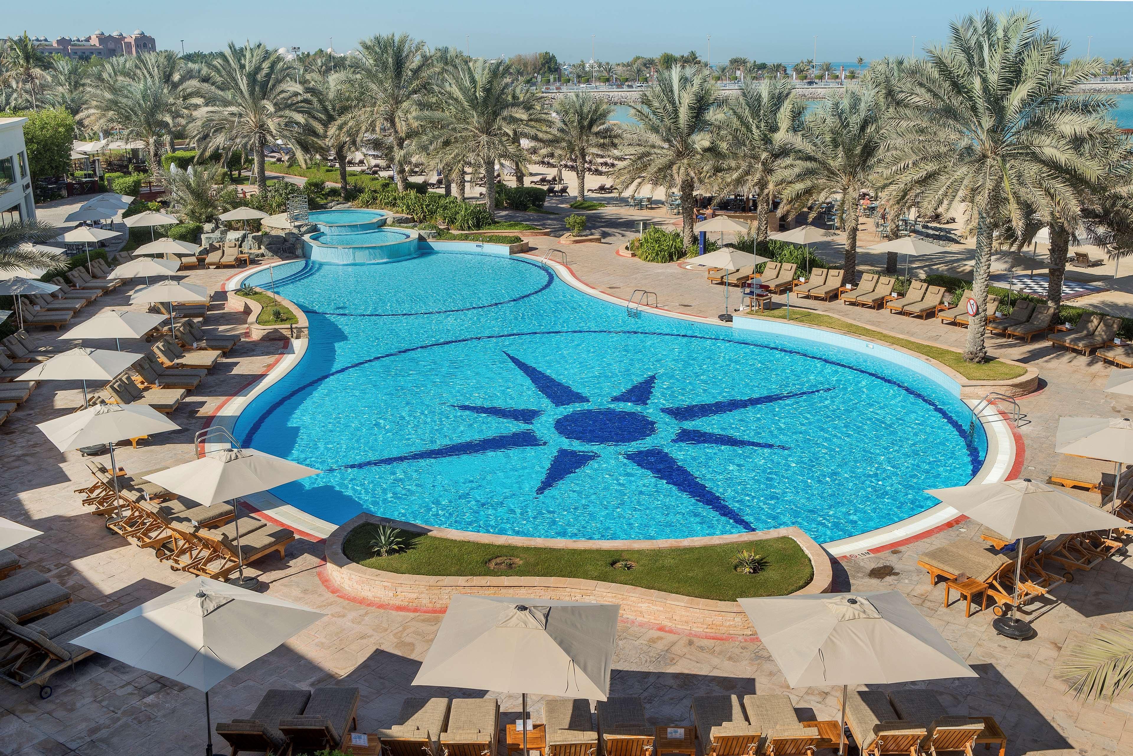 Radisson Blu Hotel & Resort, Abu Dhabi Corniche Екстериор снимка The image depicts a large, beautifully designed swimming pool shaped like a freeform design, featuring a prominent star pattern at its center. Surrounding the pool are numerous lounge chairs with light-colored cushions and umbrellas, providing shade.