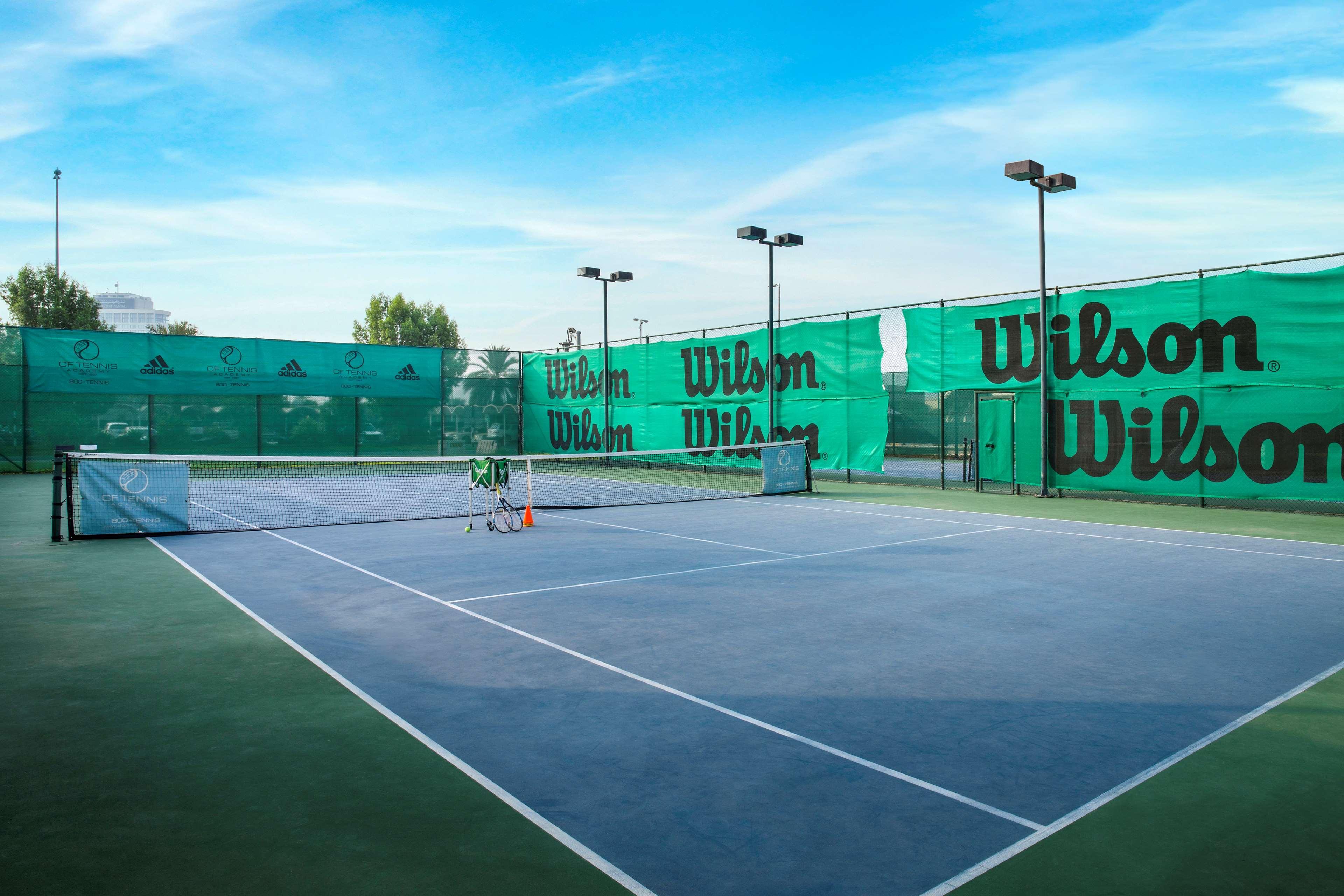 Radisson Blu Hotel & Resort, Abu Dhabi Corniche Екстериор снимка The photo shows a view of a tennis court surrounded by green nets and fencing featuring the brand name "Wilson." The court itself has a hard surface with marked lines for play. There are several tennis equipment items, such as a few rackets and possi