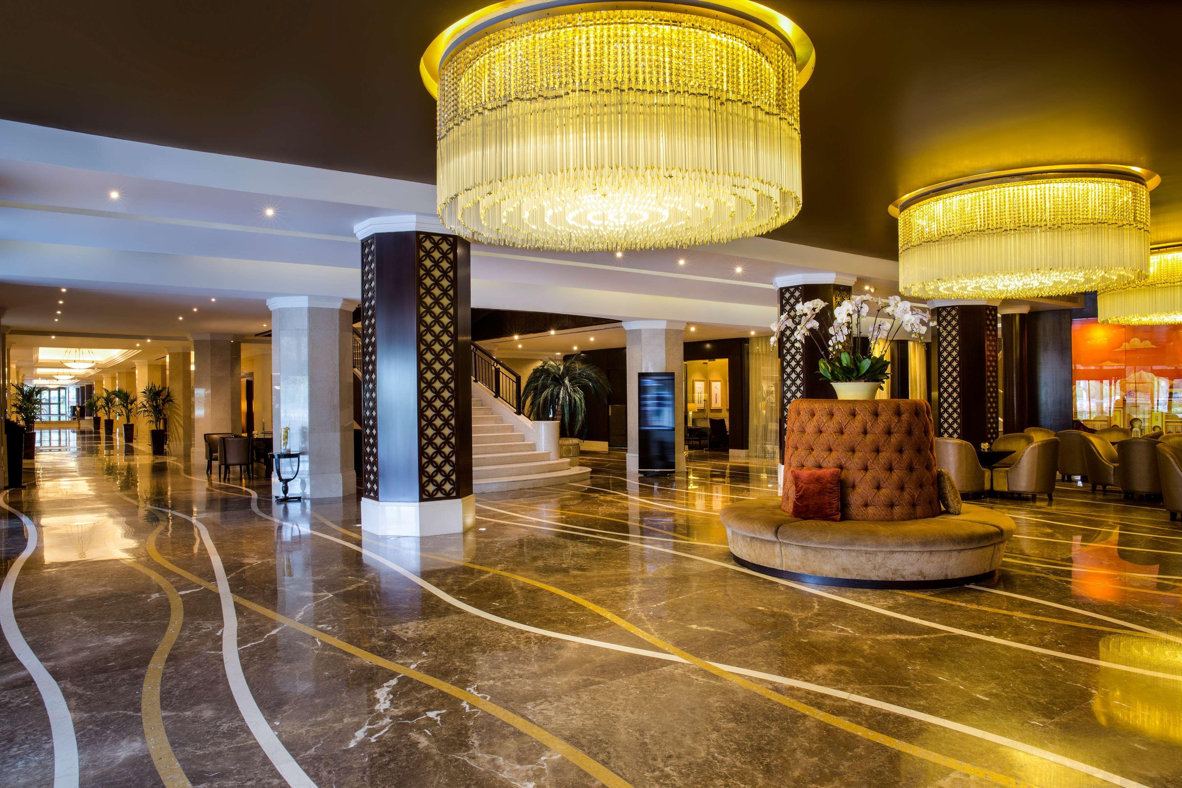 Radisson Blu Hotel & Resort, Abu Dhabi Corniche Екстериор снимка The photo depicts an elegant hotel lobby with a luxurious ambiance. The flooring is made of polished marble, featuring decorative swirling lines. There are two large, ornate chandeliers hanging from the ceiling, providing warm lighting. Column suppor