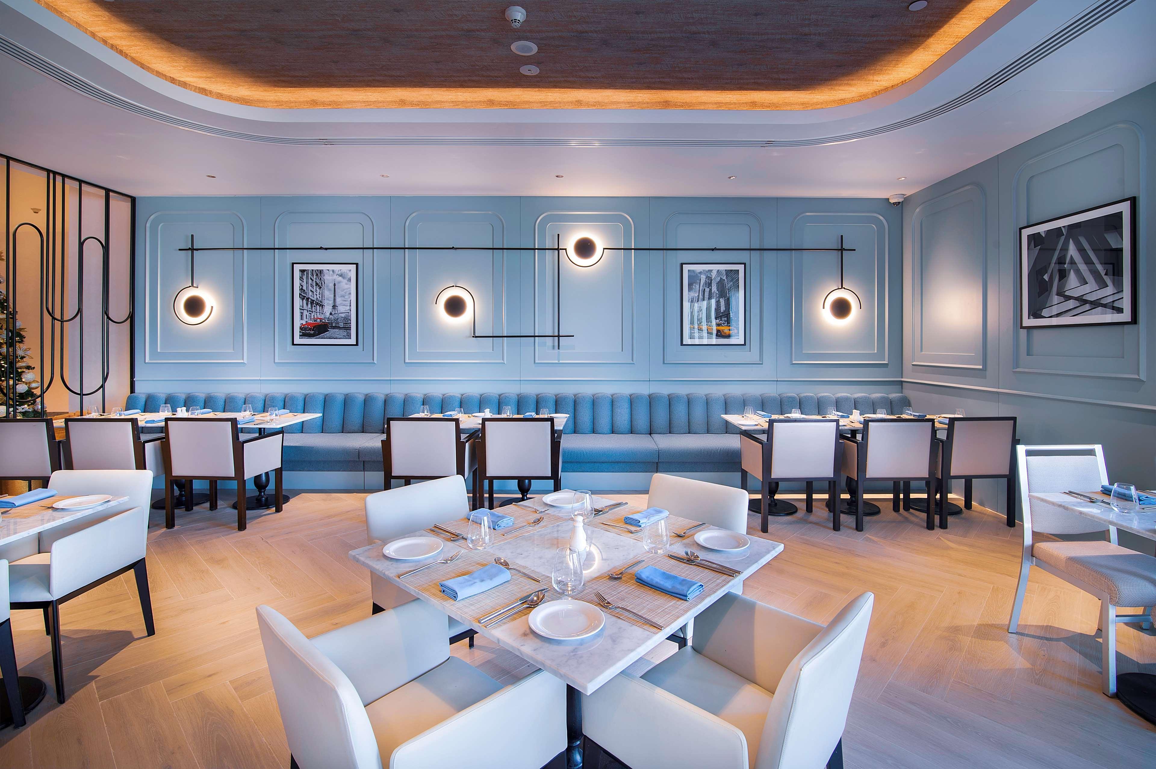 Radisson Blu Hotel & Resort, Abu Dhabi Corniche Екстериор снимка The photo shows a modern restaurant interior. The walls are painted in a soft blue, complemented by a decorative paneling design. There are multiple circular light fixtures hanging from the ceiling, providing ambient lighting. The seating includes a 