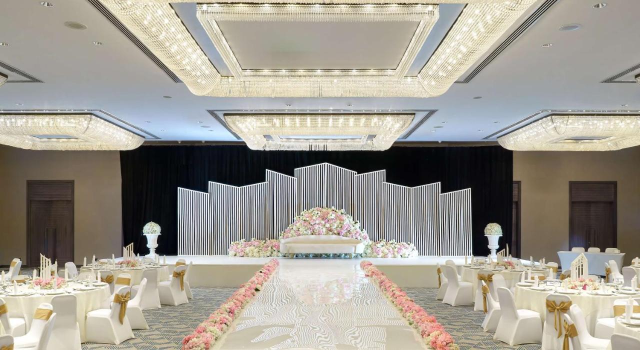 Radisson Blu Hotel & Resort, Abu Dhabi Corniche Екстериор снимка The photo depicts a beautifully arranged wedding or event venue. In the center, there is a stage adorned with decorative elements, including a backdrop made of white and silver panels and a floral arrangement featuring pastel-colored flowers. The ais