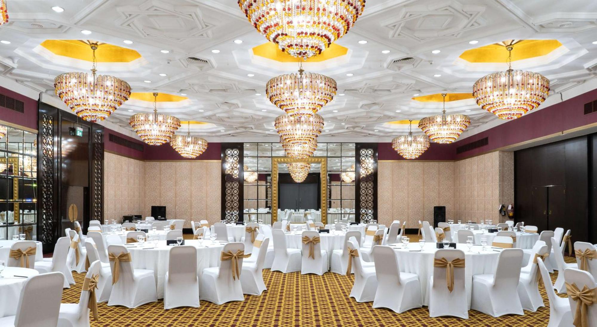 Radisson Blu Hotel & Resort, Abu Dhabi Corniche Екстериор снимка The photo depicts an elegant banquet hall or event space. The room is adorned with multiple large, ornate chandeliers that provide bright, ambient lighting. The tables are set with white tablecloths and chairs covered in white fabric, each decorated 
